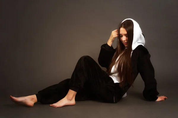 portrait of a brunette girl in the Studio on a plain black background in black and white pajamas with a hood