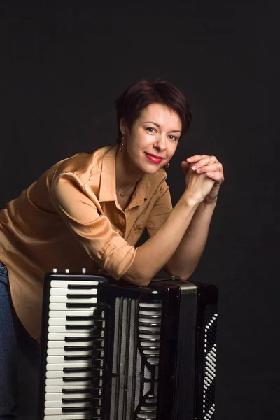 A brunette in a gold shirt, with a short haircut, on a dark background of the Studio. With accordion musician