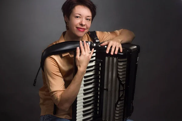 A brunette in a gold shirt, with a short haircut, on a light gray background of the Studio. With accordion musician