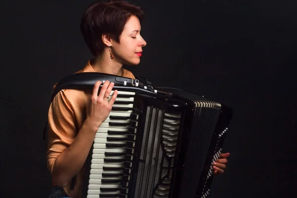A brunette in a gold shirt, with a short haircut, on a dark background of the Studio. With accordion musician