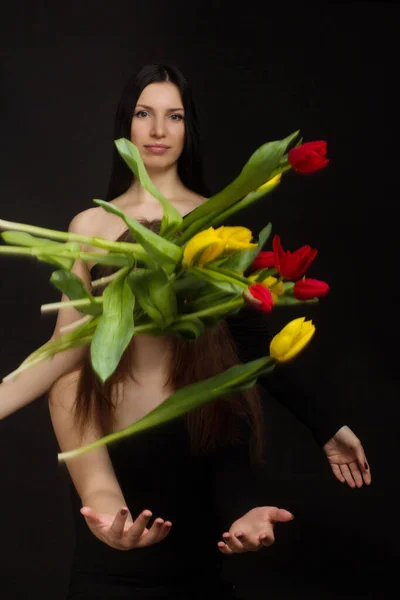 Portrait of girl and woman, mother and daughter, in a black one-shoulder dress open, naked , with red and yellow tulips, in Studio on black background. flying, falling flowers