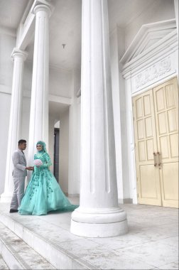 TARAKAN, INDONEZYA - 19 Şubat 2017: Endonezyalı gelin ve damat çiftlerinin beyaz binada yeşil Müslüman elbiseler giydikleri düğün öncesi fotoğraf çekimi