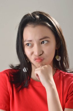 Asyalı güzel bir Çinli kız, beyaz bir fırın fotoğraf stüdyosunda yüz ifadesi ile kırmızı günlük giyinmiş.