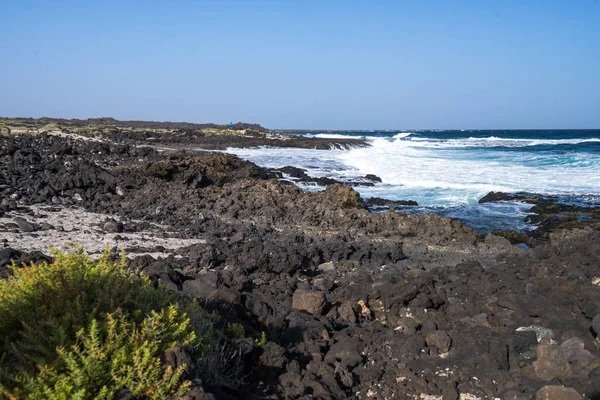 Zwarte vulkaan stenen en wit zand aan de kust — Stockfoto