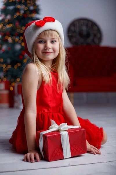 Niedliches kleines Mädchen mit Geschenk. Kind hält eine magische Geschenkbox in der Nähe des Weihnachtsbaums drinnen. — Stockfoto