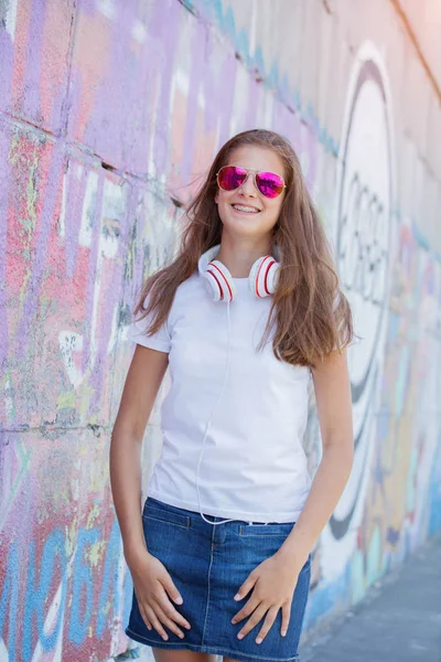 Chica vistiendo camiseta blanca en blanco, jeans posando contra la pared de la calle áspera — Foto de Stock