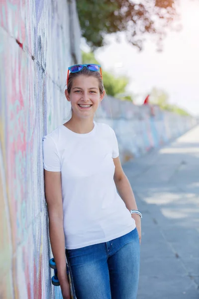 Chica vistiendo camiseta blanca en blanco, jeans posando contra la pared de la calle áspera — Foto de Stock