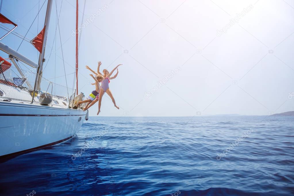 Boy with his sister jump of sailing yacht on summer cruise. Travel adventure, yachting with child