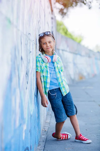 Χαριτωμένο αγόρι με skateboard σε εξωτερικούς χώρους, που στέκεται στο δρόμο με διαφορετικά πολύχρωμα γκράφιτι στους τοίχους — Φωτογραφία Αρχείου