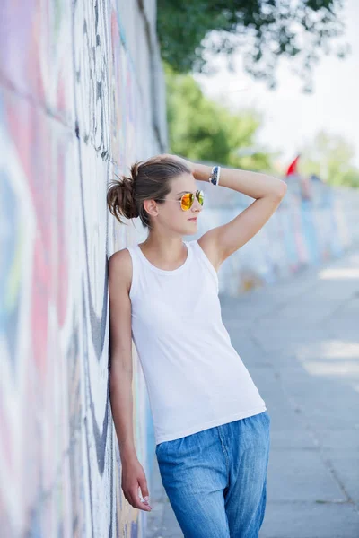 Meisje met lege witte t-shirt, jeans poseren tegen ruwe straat muur — Stockfoto