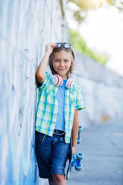 Cute boy with skateboard outdoors, standing on the street with different colorful graffiti on the walls — Stock Photo, Image