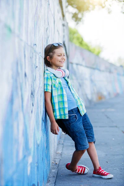 Симпатичный мальчик со скейтбордом на открытом воздухе, стоит на улице с различными красочными граффити на стенах — стоковое фото