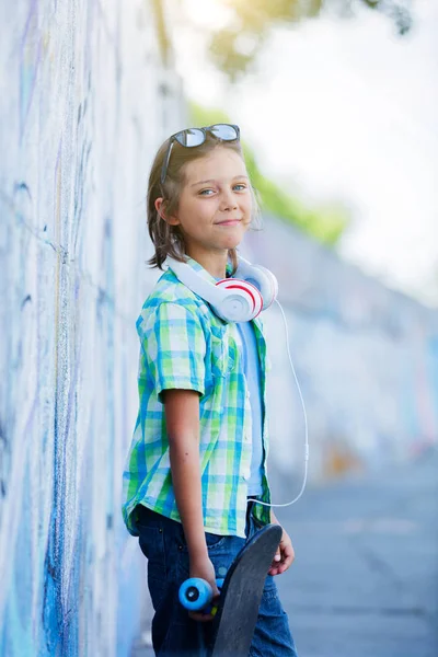 야외에서, 스케이트 보드와 다른 다채로운 낙서 벽에 거리에 서 있는 귀여운 소년 — 스톡 사진