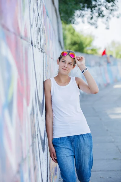 Ragazza che indossa bianco t-shirt, jeans in posa contro muro di strada grezzo — Foto Stock