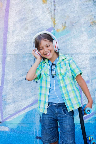 Carino ragazzo con skateboard all'aperto, in piedi sulla strada con diversi graffiti colorati sulle pareti — Foto Stock