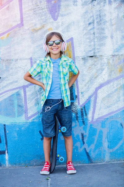 Carino ragazzo con skateboard all'aperto, in piedi sulla strada con diversi graffiti colorati sulle pareti — Foto Stock