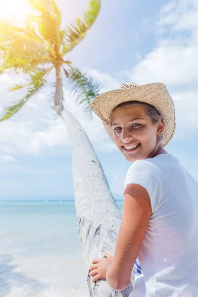 Gelukkig meisje zit op een palmboom in een tropisch strand — Stockfoto