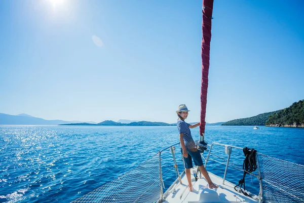 Kleine jongen aan boord van zeiljacht op zomercruise. Reis avontuur, zeilen met kind op vakantie met het gezin. Stockfoto