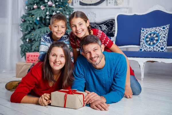 Pais e duas crianças fofas se divertindo perto da árvore de Natal dentro de casa . — Fotografia de Stock