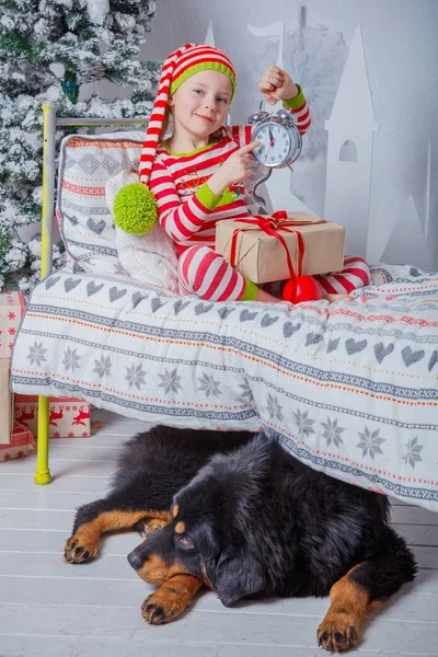 自宅内装の新年の部屋に座っている縞模様のパジャマを着た幸せなかわいい女の子. — ストック写真