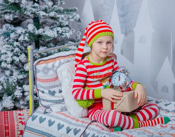 Счастливая симпатичная маленькая девочка в полосатой пижаме сидит дома в украшенной новогодней комнате . — стоковое фото
