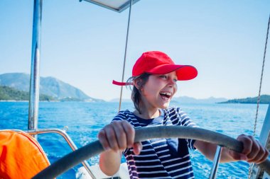 Little boy captain on board of sailing yacht on summer cruise. Travel adventure, yachting with child on family vacation. clipart