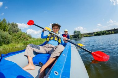 Mutlu çocuk yaz tatilinde güneşli bir günde nehirde kano yapıyor.