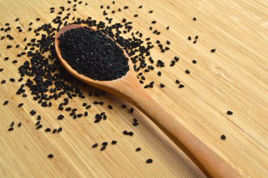 Tahta kaşıkta, bambu kesme tahtasının üzerinde bir sürü kuru siyah kimyon.