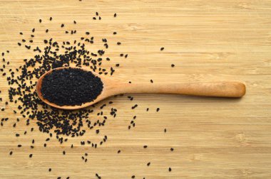 Tahta kaşıkta, bambu kesme tahtasının üzerinde bir sürü kuru siyah kimyon.