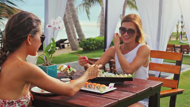 Två damer äta sushi rullar på stranden — Stockvideo