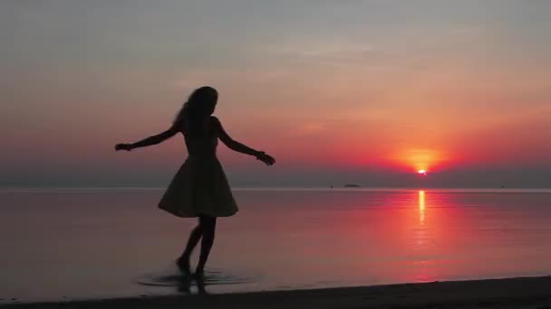 Счастливая молодая женщина, виляющая на пляже на закате — стоковое видео