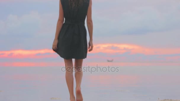 Gün batımında sahilde yürüyen genç bir kadın — Stok video