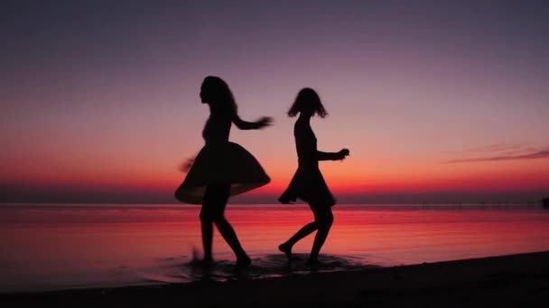 Dos chicas felices girando y bailando en la playa al atardecer — Vídeo de stock