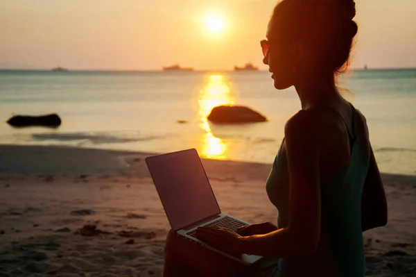 Dame avec un ordinateur portable sur la plage au coucher du soleil — Photo