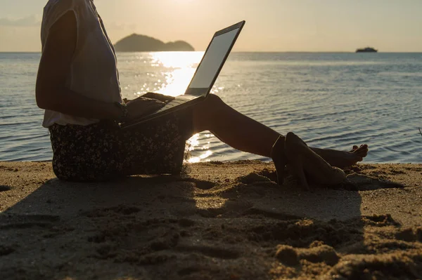 Dame avec un ordinateur portable sur la plage au coucher du soleil — Photo
