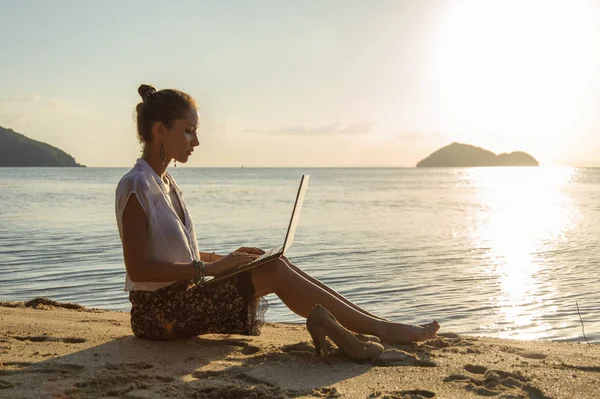 Pani z laptopa na plaży o zachodzie słońca — Zdjęcie stockowe