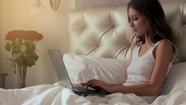 Jonge vrouw die op laptop in bed werkt — Stockvideo