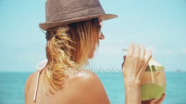 Kadın içki taze hindistan cevizi su ile saman plaj tatil eğlenceli. Yaz tatili sırasında sağlıklı snack için yudumlarken genç yeşil tropikal meyve tutan kadın closeup