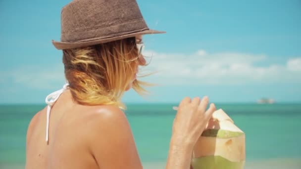 Kvinna dricka färsk kokosvatten med sugrör på stranden kul semester. Närbild av kvinna med ung grön tropisk frukt smuttar för hälsosamt mellanmål under sommarlovet — Stockvideo