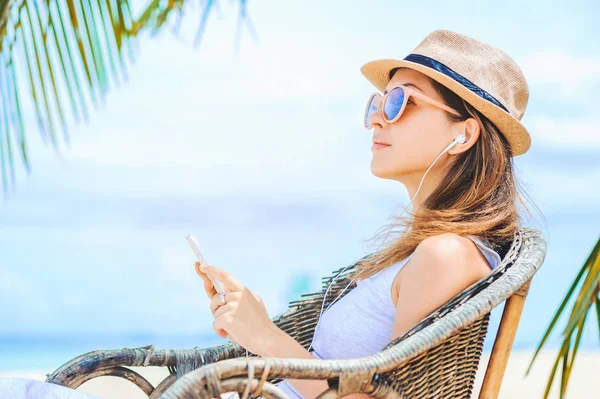 Jonge sexy vrouw met koptelefoon met behulp van de telefoon op het strand — Stockfoto