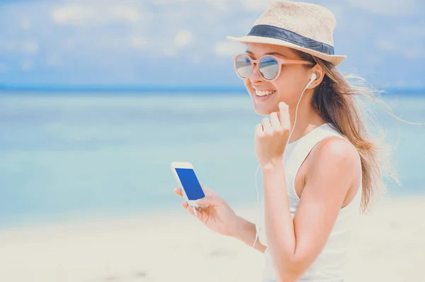 Jonge sexy vrouw met koptelefoon met behulp van de telefoon op het strand — Stockfoto