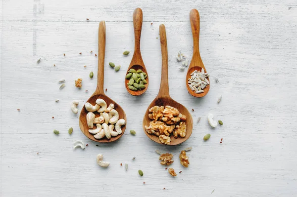 Cucharas de madera con semillas y nueces en la mesa blanca —  Fotos de Stock