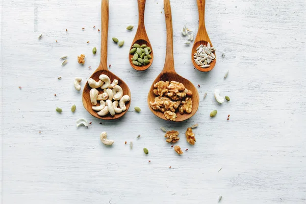 Cucharas de madera con semillas y nueces en la mesa blanca —  Fotos de Stock