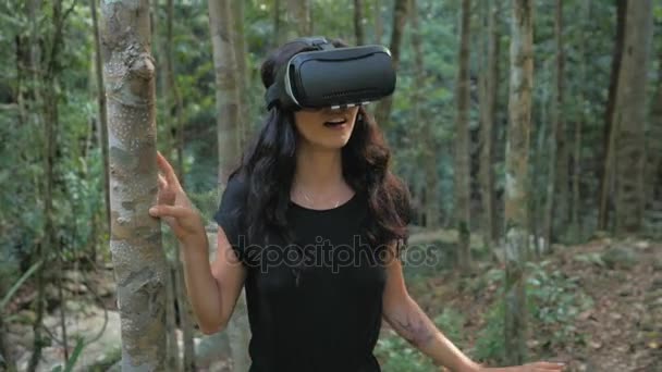 Красивая молодая брюнетка женщина использует очки виртуальной реальности в джунглях — стоковое видео