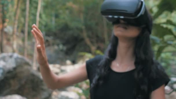 Hermosa joven morena mujer utiliza gafas de realidad virtual en la selva — Vídeo de stock