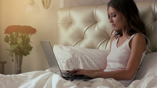 Молодая женщина работает на ноутбуке в постели 2 выстрелов — стоковое видео