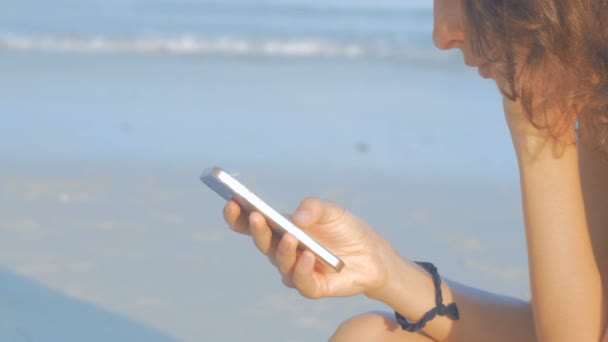 Kvinna textning med sin telefon på stranden — Stockvideo