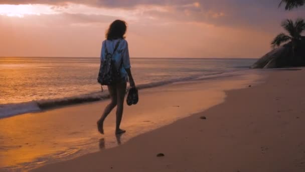 Kobieta z plecaka spaceru na plaży, w zachód słońca, światła, steadicam strzał — Wideo stockowe