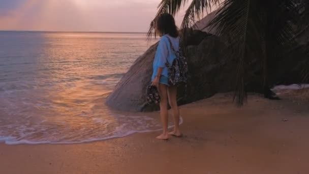 Mulher com mochila andando na praia, em luz do pôr do sol, steadicam tiro — Vídeo de Stock