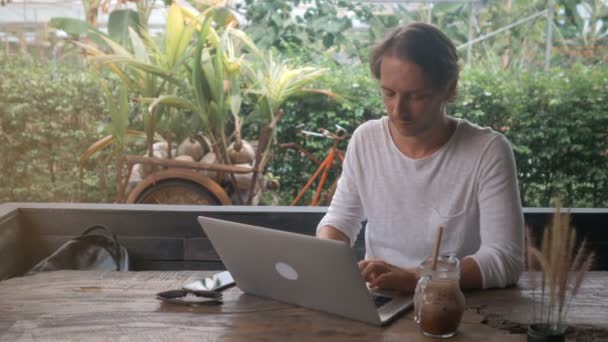 Молодой человек фрилансер, работающий на ноутбуке в кафе на открытом воздухе — стоковое видео